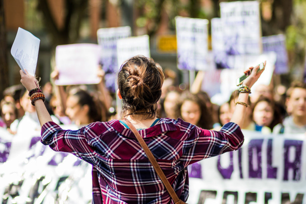 Jeune femme de dos prend parole devant un groupe de jeunes manifestants.